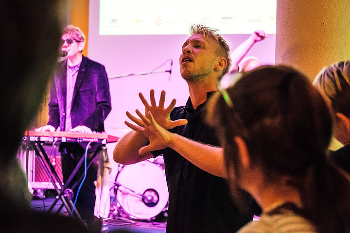 Konzert der Band Rudely Interrupted Im Hintergrund spielt die Band Rudely Interrupted, im Vordergund übersetzt ein Dolmetscher den Songtext in Australische Gebärdensprache