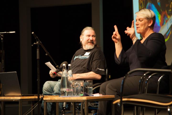 Präsentation Andrew Hewitt Links Andew Hewitt, lachend, rechts eine DGS-Dolmetscherin