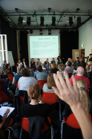 Workshop "Money matters - Geldangelegenheiten" Sicht von hinten auf die Zuschauer*innen in Reihen, vorne eine Powerpoint-Präsentation