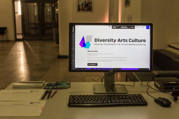 Auf einem Tisch steht ein Computer, der Bildschirm zeigt die Webseite von Diversity Arts Culture