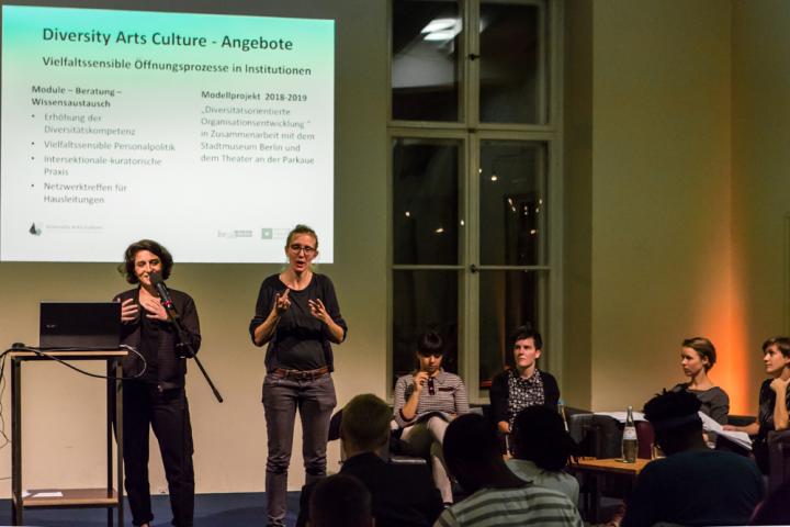 Eine Mitarbeitende von Diversity Arts Culture präsentiert ihren Arbeitsbereich.