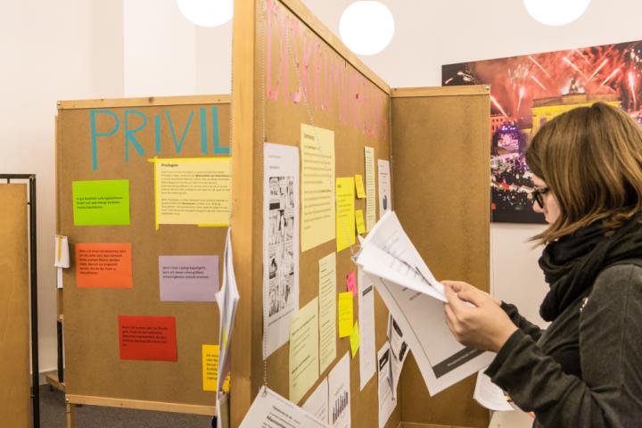 Eine Frau liest einen Artikel, der an einer Stellwand befestigt ist, auf der groß Diskriminierung steht.