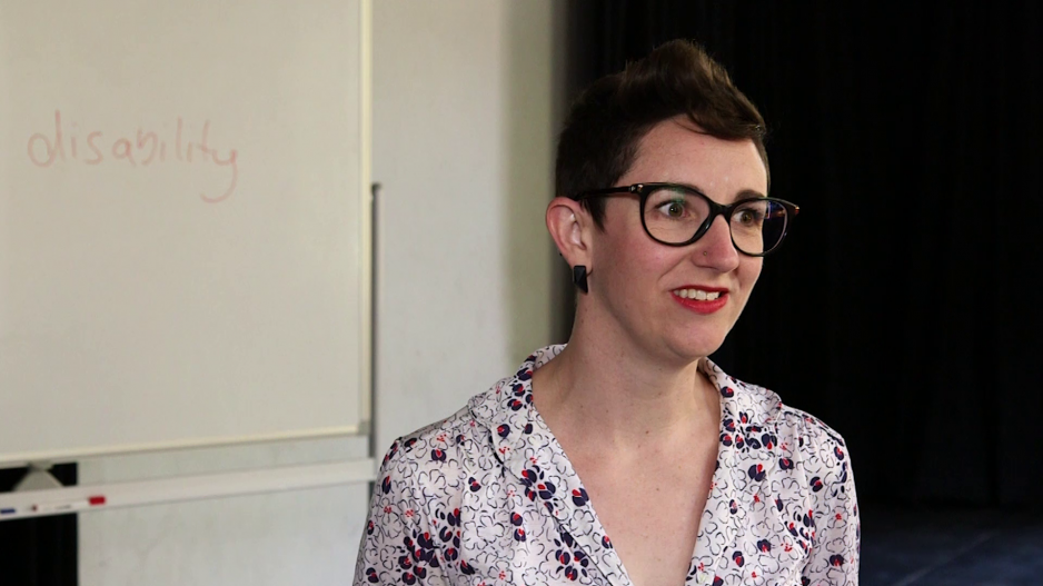 Kate Brehme steht vor einem Whiteboard, auf dem das Wort disability zu lesen ist