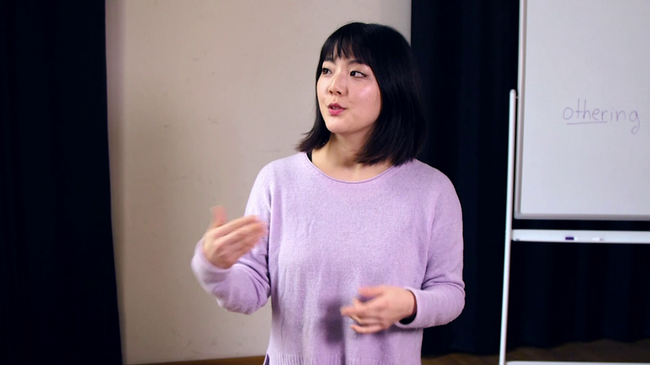 Olivia Hyunsin Kim steht vor einem Whiteboard, auf dem Othering steht