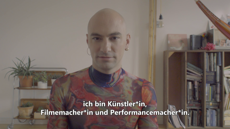 Simon(e) Jaikiriuma Paetau im Halbporträt. Simon(e) trägt ein buntes Oberteil und Ohrringe.