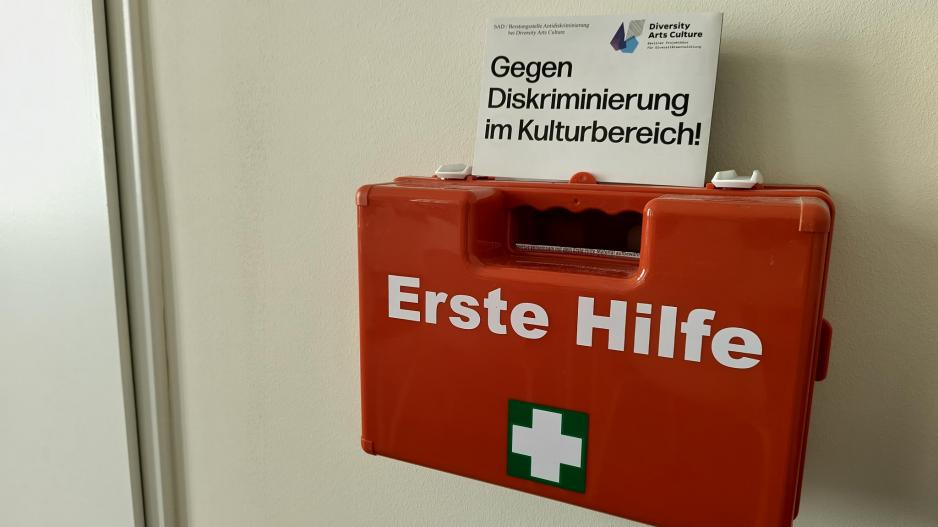 Roter erste Hilfe Kasten auf dem ein Flyer von Diversity Arts Culture steht mit dem Schriftzug "Gegen Diskriminierung im Kulturbereich"